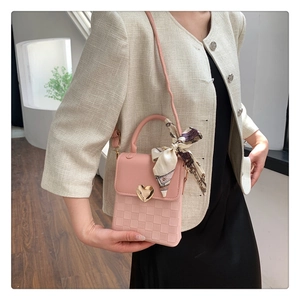 Close-up of pink crossbody bag with heart buckle, checkered texture, and silk scarf handle