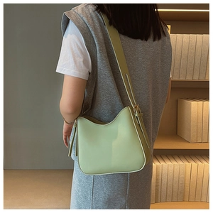 Gros plan d'un sac besace en cuir vert clair avec bandoulière large sur un modèle
