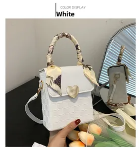 Detailed view of white checkered handbag featuring golden heart clasp and silk scarf handle
