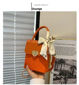 Close-up of orange crossbody bag with checkered texture and gold heart buckle