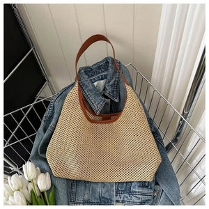 Gros plan d'un sac de plage en paille tressée avec poignées en cuir marron sur denim