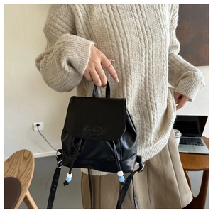Détail du mini sac à dos en cuir noir avec texture litchi et cordon à perles