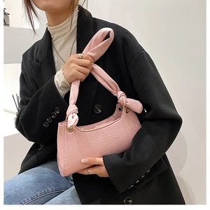 Close-up of pink faux crocodile skin texture and knotted handle on a crescent handbag
