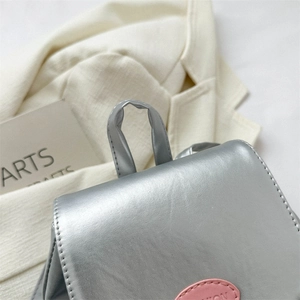 Détail du mini sac à dos argenté métallisé avec étiquette rose et texture de la poignée