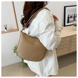 Close-up of light brown pebbled leather shoulder bag shown on a model in white shirt