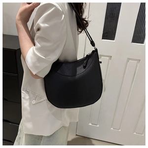 Close-up of a black textured leather hobo bag worn by a model in a white blazer