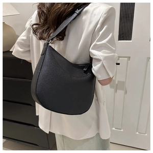 Detail of minimalist black pebble leather crescent saddle bag worn as an underarm shoulder bag