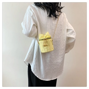 Détail du sac seau jaune clair avec nœud et broderie cœur sur une chemise blanche