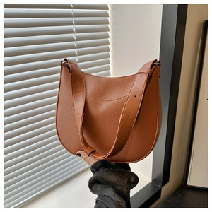 Detail of lychee-textured leather saddle bag with adjustable strap and metal hardware