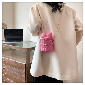 Sac cylindre rose avec matelassage cœur, nœud et chaîne dorée sur veste blanche