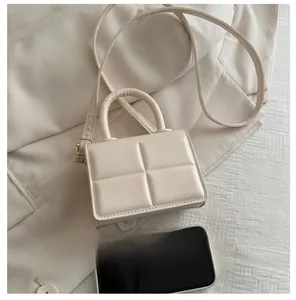 Detail view of a cream quilted micro handbag with an adjustable strap on white fabric