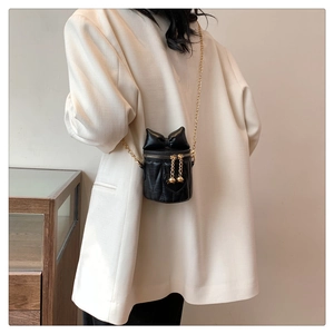 Détail du mini sac cylindre noir avec surpiqûres en cœur, nœud et bandoulière chaîne