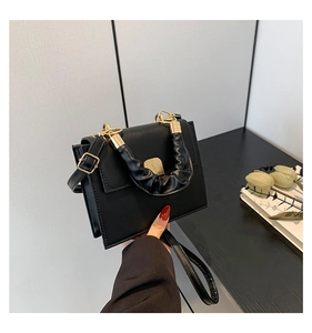Detailed view of black matte leather handbag with gold hardware and ruffled cloud handle