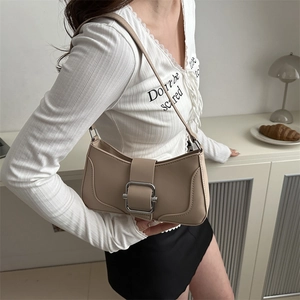 Minimalist beige baguette shoulder bag with large silver buckle on simple interior background