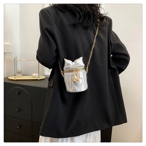 Sac seau matelassé argenté avec nœud et bandoulière chaîne porté sur un blazer noir
