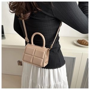 Detail of beige puffer crossbody bag showing quilted texture and golden hardware accents