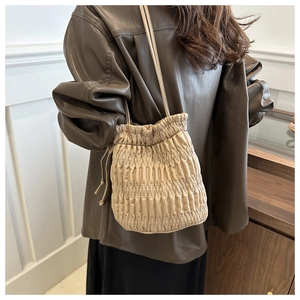 Detail of beige pleated drawstring bucket bag with a crossbody strap on a lifestyle model