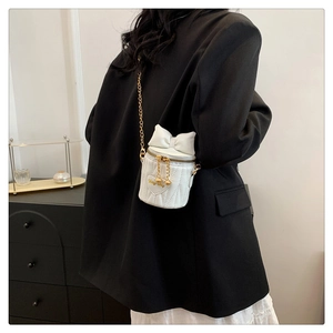 Détail d'un sac seau blanc matelassé avec nœud en cuir et chaîne dorée