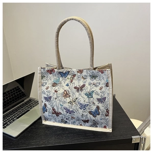Detail van beige canvas draagtas met kleurrijk vlinderborduurwerk en stevige touwhandvatten
