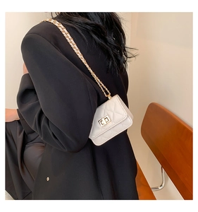 White quilted mini crossbody bag with gold chain strap worn over a black blazer