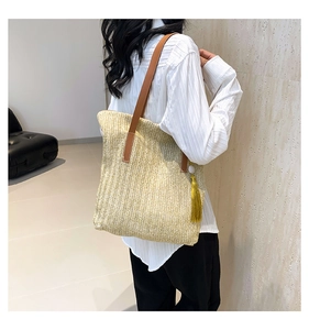 Detail of large woven tote bag with brown leather straps and yellow tassel accessory