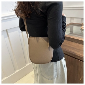 Detail view of large grey leather crossbody bucket bag worn on shoulder by model