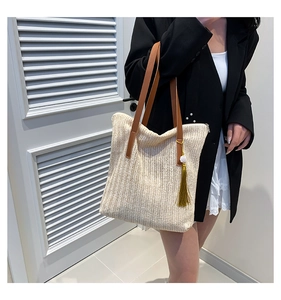 Détail du sac cabas tressé beige avec bandoulière en cuir marron et pompon doré