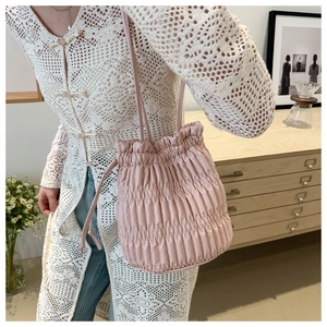 Gros plan du sac seau plissé rose porté avec un gilet en dentelle blanche élégant