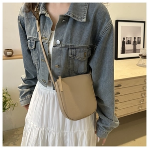 Beige litchi-grain leather saddle crossbody bag shown on model in a casual lifestyle setting