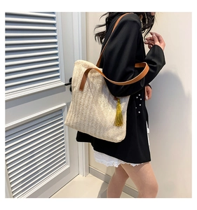 Detail of straw bucket bag featuring woven texture, leather strap and yellow tassel