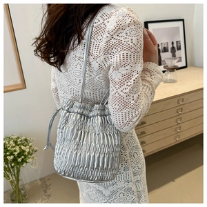 Sac seau matelassé argenté porté à l'épaule dans un décor minimaliste et chaleureux de mode