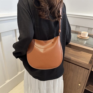 Minimalist brown lychee leather saddle bag with adjustable strap worn by a woman