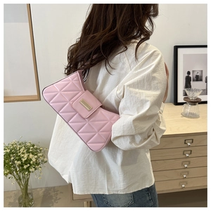 Detalle de bolso baguette rosa acolchado con placa dorada usado por modelo en un interior