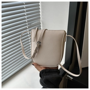 Close-up of beige lychee grain leather crossbody bag with adjustable silver buckle strap