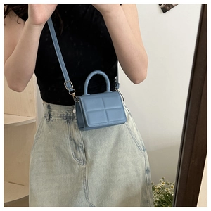 Close-up of a light blue quilted mini handbag featuring golden metal strap buckles