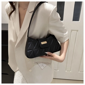 Detalle de bolso acolchado negro con hebilla dorada sobre una chaqueta beige