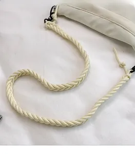 Detail of a creamy white nylon bag featuring a spiral woven rope shoulder strap and metal buckle
