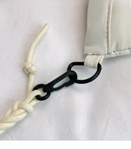 Detail of detachable braided rope strap with black metal clasp on beige quilted bag