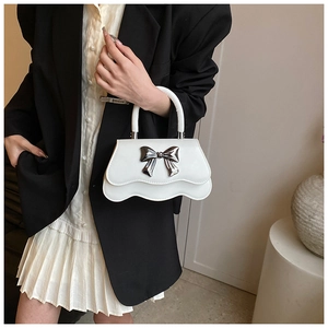 Detail of white handbag with silver metal bow and wavy bottom edge on a model