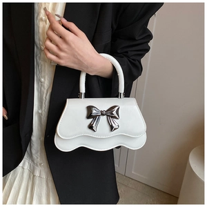 Close-up of white crossbody bag with silver bow ornament and scalloped bottom edge
