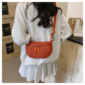 Detail of an orange crescent nylon bag featuring thick braided straps on a female model