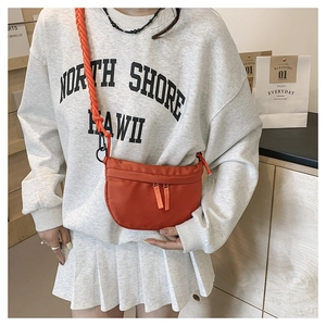 Detail view of a bright orange crossbody bag with woven strap and dual zipper pockets
