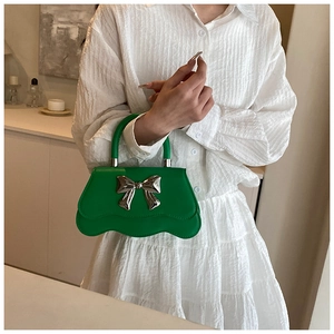Detail of green shoulder bag with wavy base and silver bow buckle on white shirt
