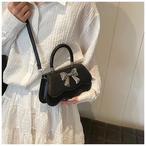 Close-up of a black handbag with a silver metal bow and wavy bottom edge on a model