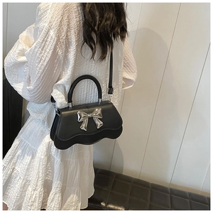Detail view of a black wavy bottom handbag with silver bow and leather chain strap