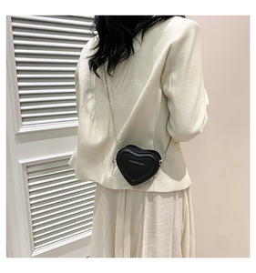 Close-up of heart-shaped black crossbody bag with gold lettering and silver chain strap