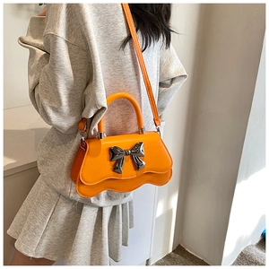 Detail of bright orange handbag with wave-cut base and silver bow on grey outfit