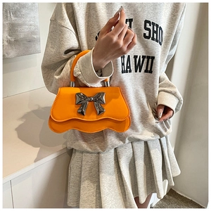 Detail view of bright orange wavy base handbag with silver metal bow and top handle