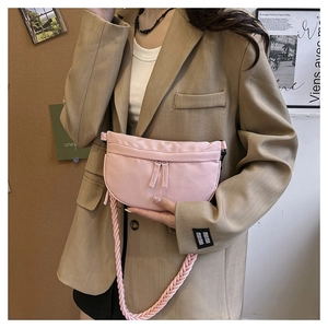 Detail of pink half-moon crossbody bag with woven strap and dual zipper closure on a model