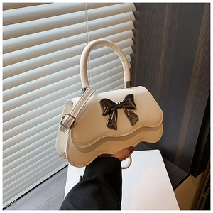 Detail of cream white handbag featuring wavy flap and large dark metallic bow accent